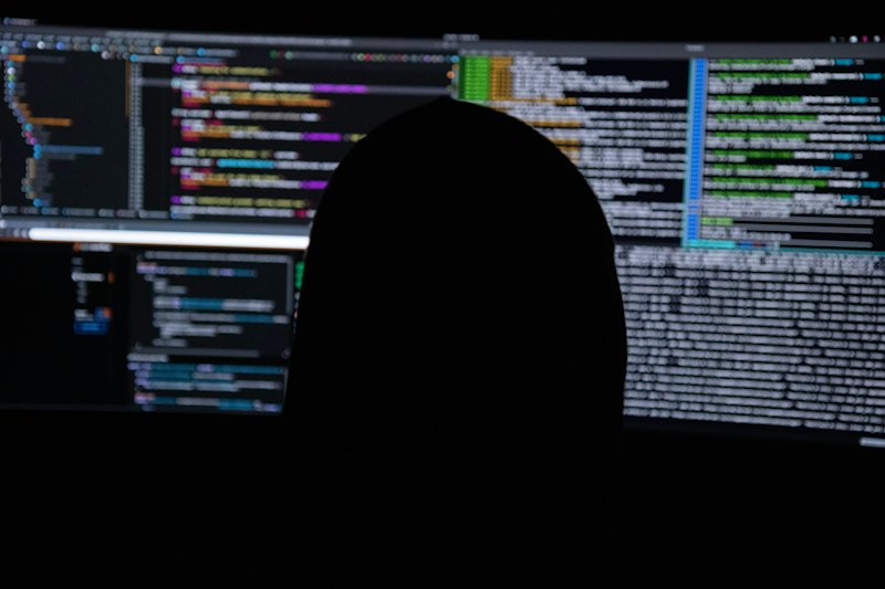 Pessoa em silhueta diante de monitores com código